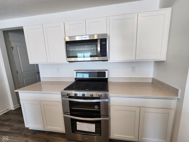 kitchen featuring light stone countertops, appliances with stainless steel finishes, white cabinets, and dark wood-style flooring