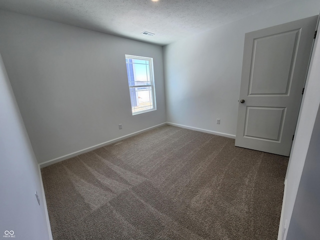 empty room featuring a textured ceiling, dark carpet, visible vents, and baseboards