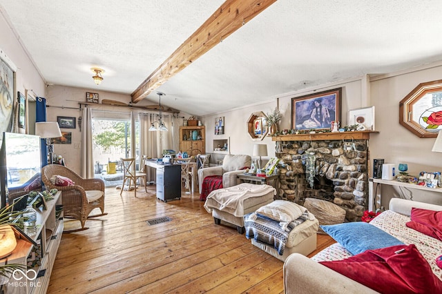 living room with a stone fireplace, vaulted ceiling with beams, hardwood / wood-style floors, and a textured ceiling