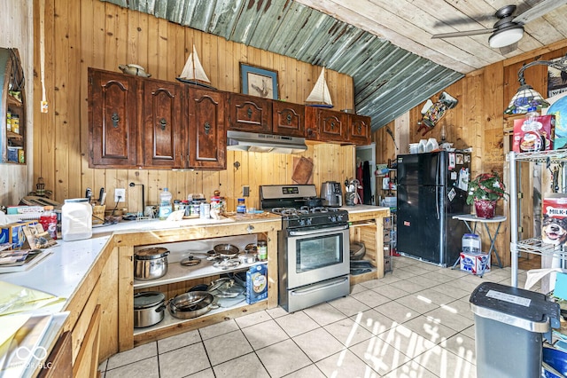 kitchen with wood walls, black fridge, vaulted ceiling, light tile patterned floors, and stainless steel range with gas cooktop