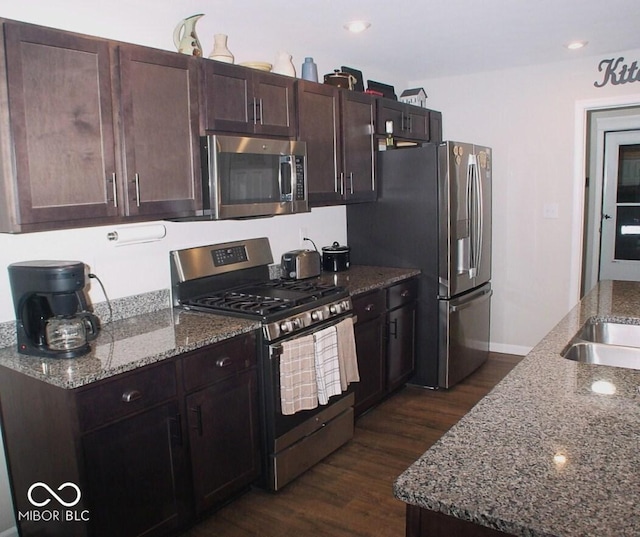 kitchen with appliances with stainless steel finishes, dark wood-type flooring, light stone counters, and dark brown cabinets