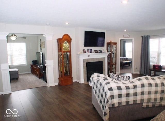 living room with dark wood-type flooring, ceiling fan, a tile fireplace, and ornate columns