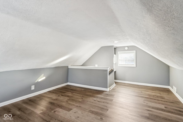 additional living space with dark wood-type flooring, lofted ceiling, and a textured ceiling