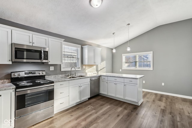 kitchen with sink, appliances with stainless steel finishes, kitchen peninsula, pendant lighting, and white cabinets