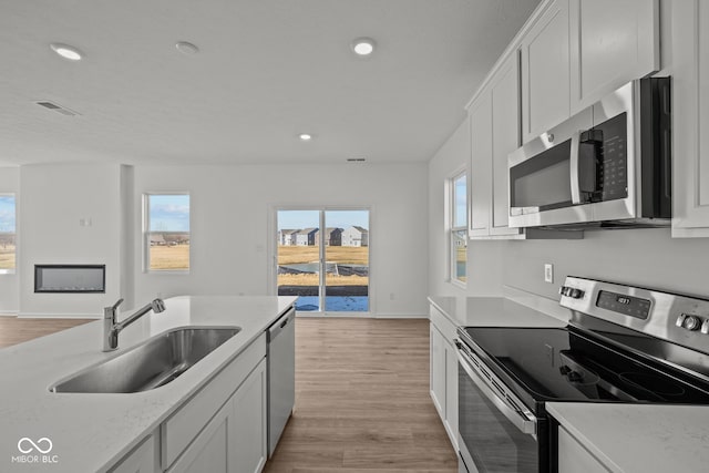 kitchen with baseboards, a sink, stainless steel appliances, white cabinets, and light wood-style floors