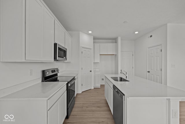 kitchen featuring a sink, light wood-type flooring, white cabinets, stainless steel appliances, and a kitchen island with sink