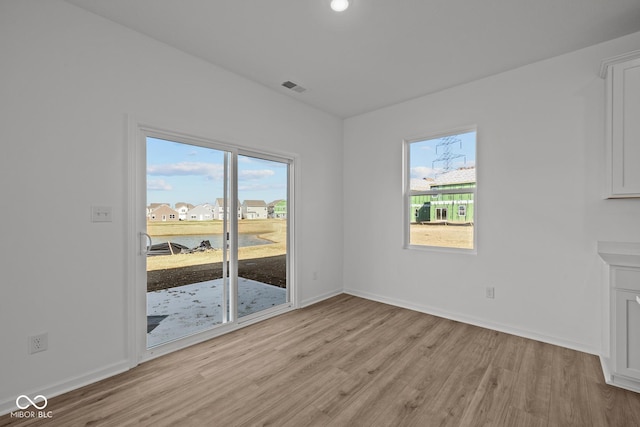 unfurnished living room featuring baseboards, visible vents, a wealth of natural light, and light wood-type flooring