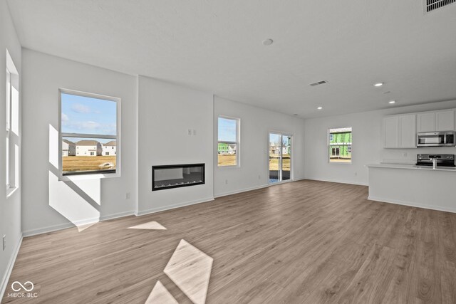 unfurnished living room featuring visible vents, light wood-style flooring, and a glass covered fireplace