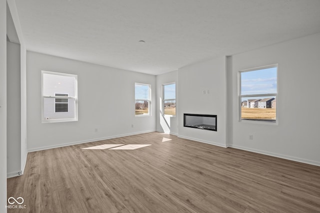 unfurnished living room with a glass covered fireplace, baseboards, and light wood-style floors