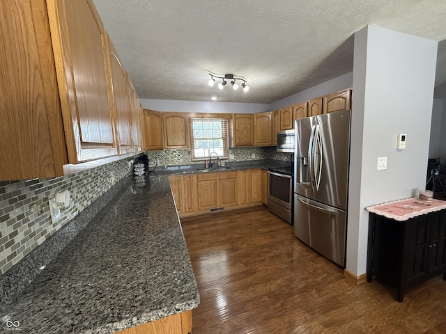 kitchen with appliances with stainless steel finishes, sink, dark stone countertops, backsplash, and dark hardwood / wood-style flooring