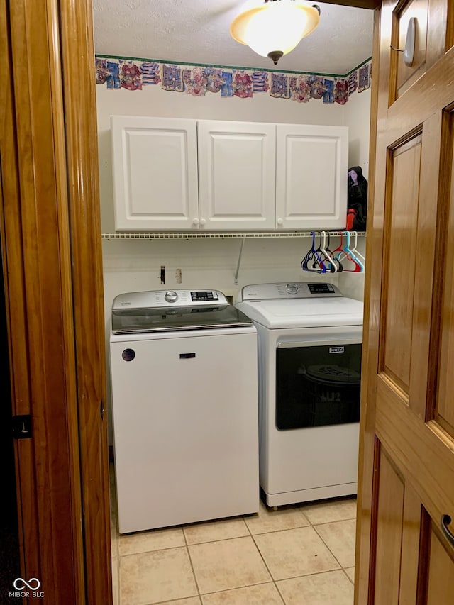 laundry area with cabinets, washing machine and dryer, a textured ceiling, and light tile patterned floors