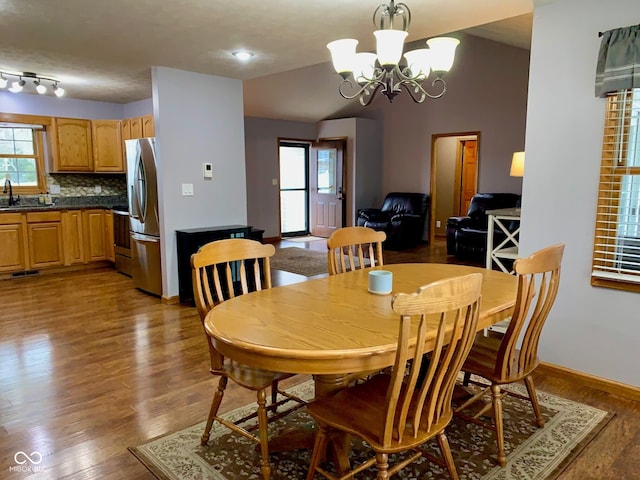 dining space featuring hardwood / wood-style flooring, vaulted ceiling, sink, and a notable chandelier