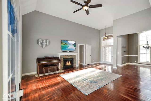 living room with dark hardwood / wood-style flooring, ceiling fan with notable chandelier, a fireplace, and high vaulted ceiling