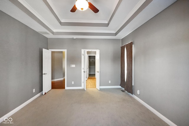 unfurnished bedroom with ceiling fan, light colored carpet, a spacious closet, and a raised ceiling