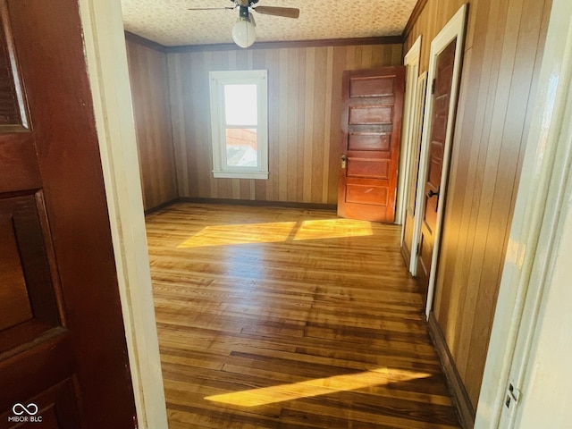 interior space featuring ceiling fan, light hardwood / wood-style floors, a textured ceiling, and wooden walls