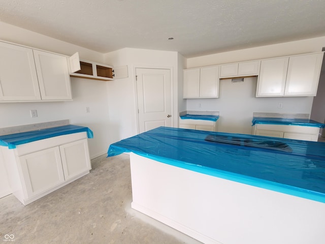 kitchen featuring a textured ceiling, white cabinets, and unfinished concrete flooring