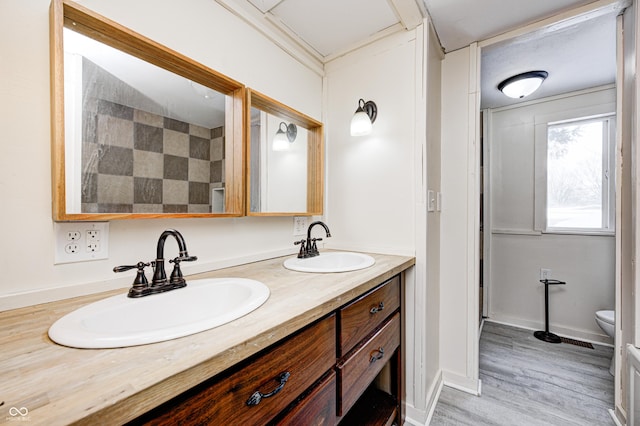 bathroom with toilet, vanity, wood-type flooring, and crown molding