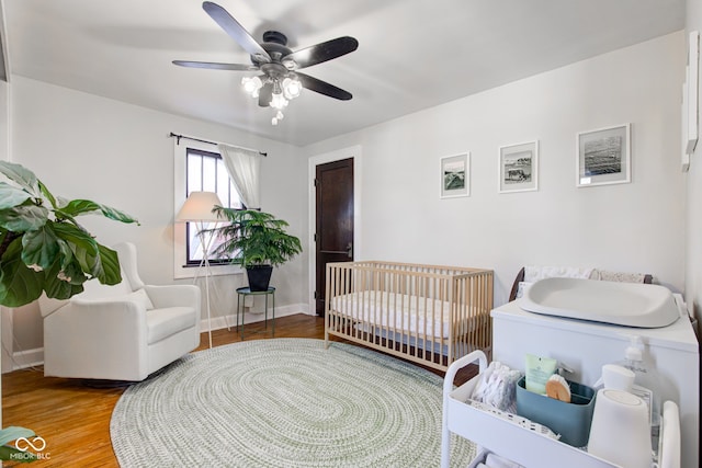 bedroom with ceiling fan, a nursery area, and hardwood / wood-style flooring