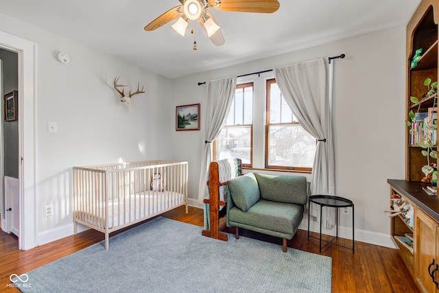 bedroom featuring dark wood-type flooring, ceiling fan, and a crib