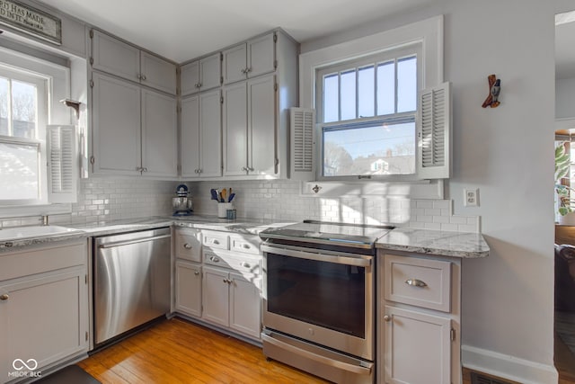 kitchen featuring light stone countertops, stainless steel appliances, tasteful backsplash, light hardwood / wood-style floors, and gray cabinetry