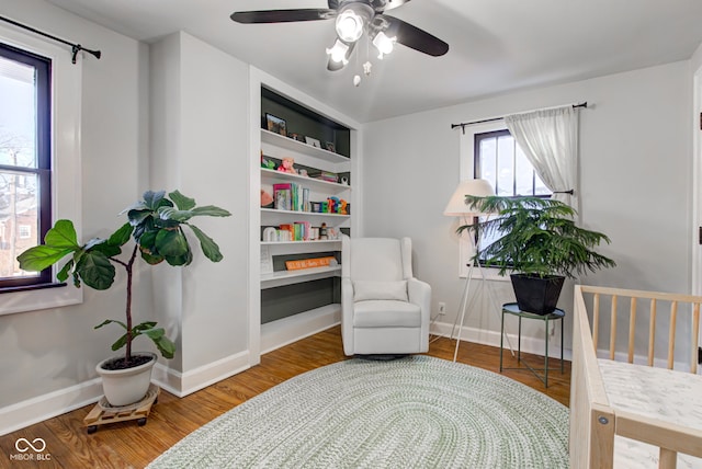 sitting room with ceiling fan, built in shelves, and hardwood / wood-style flooring