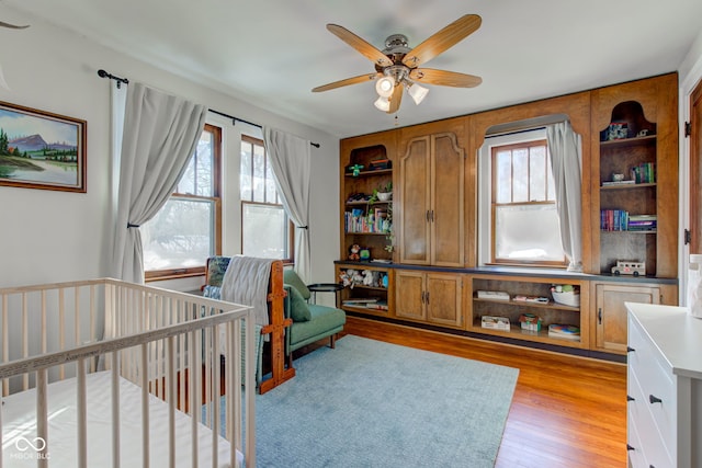 bedroom with ceiling fan, light hardwood / wood-style floors, and a crib