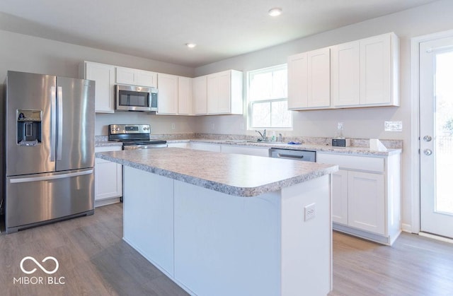 kitchen with light hardwood / wood-style flooring, sink, white cabinets, a kitchen island, and stainless steel appliances