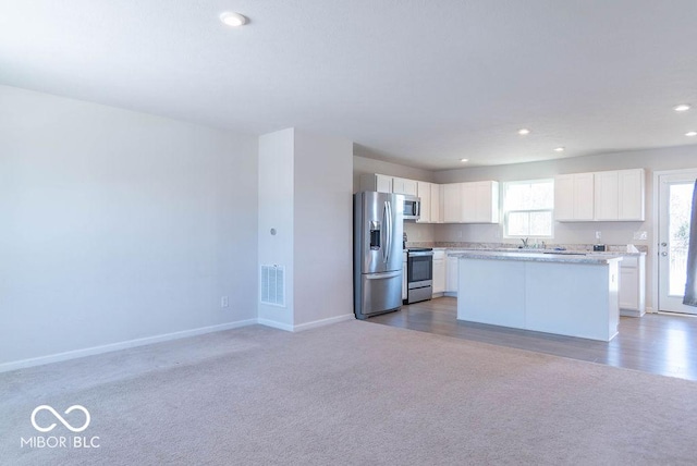 kitchen featuring light colored carpet, white cabinets, a center island, and stainless steel appliances