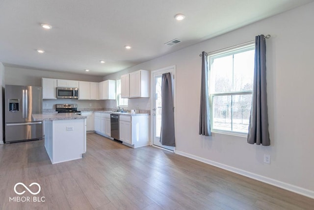 kitchen featuring light stone countertops, white cabinetry, light wood-type flooring, a kitchen island, and stainless steel appliances