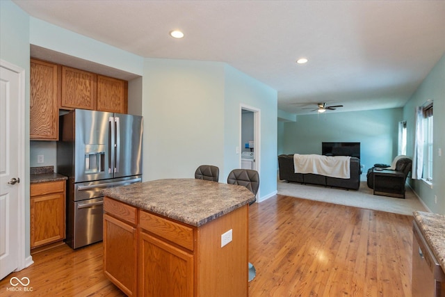 kitchen with ceiling fan, stainless steel fridge, a kitchen island, and light wood-type flooring