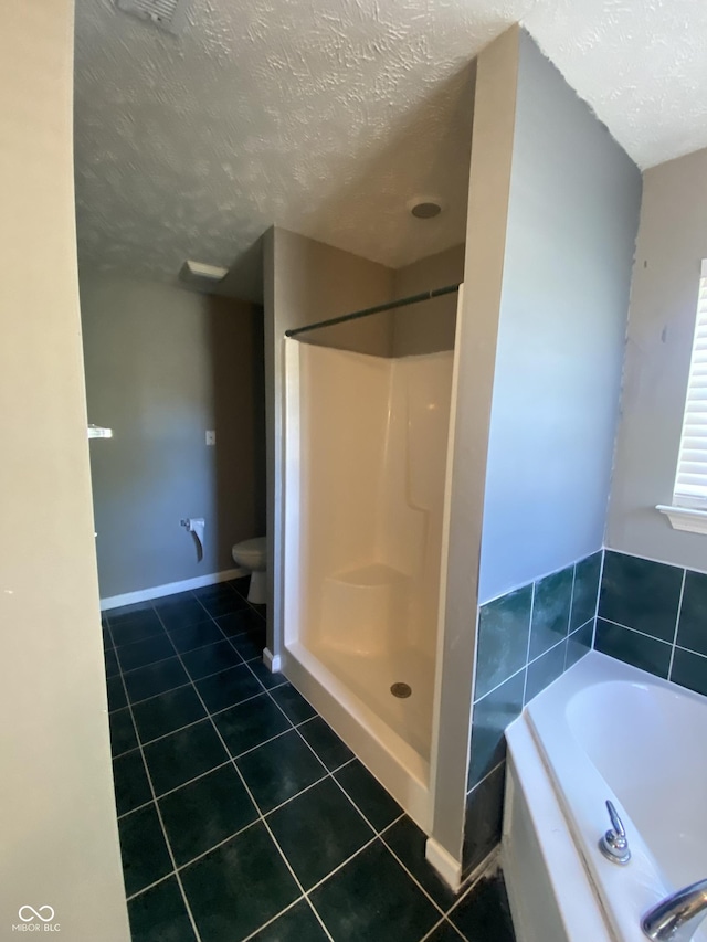 bathroom with a textured ceiling, toilet, tile patterned floors, and separate shower and tub