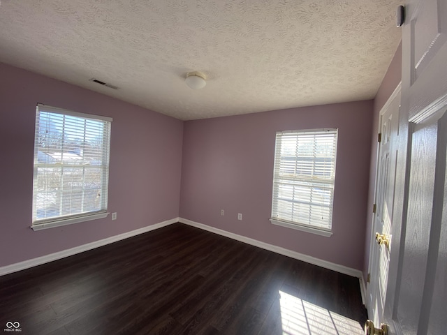 empty room with a healthy amount of sunlight, dark hardwood / wood-style flooring, and a textured ceiling