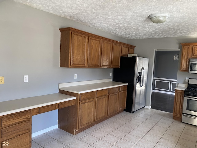 kitchen featuring built in desk, light tile patterned floors, stainless steel appliances, and a textured ceiling