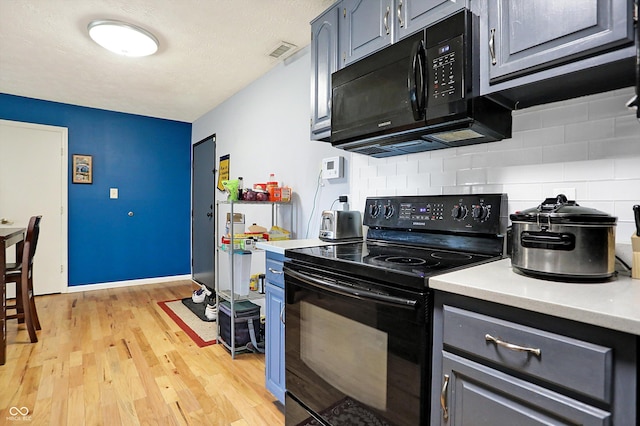 kitchen featuring light wood-type flooring, decorative backsplash, and black appliances