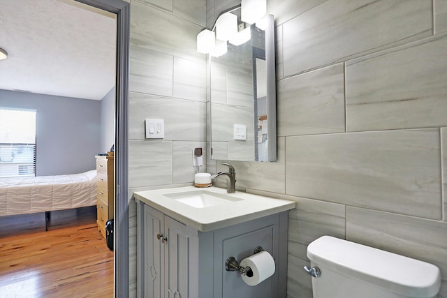 bathroom featuring vanity, wood-type flooring, tile walls, and toilet