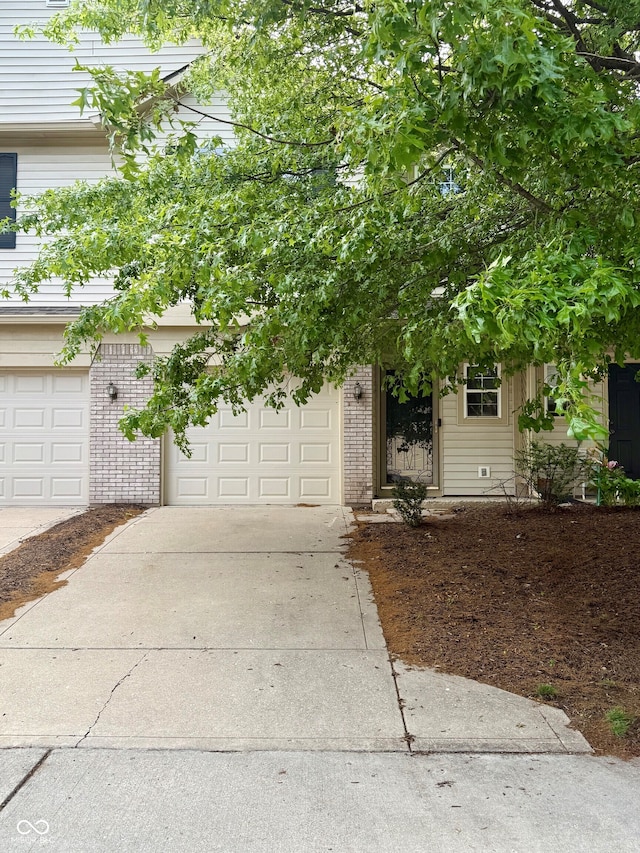 7042 Tyler Ln, Indianapolis, IN 46217 - view of property hidden behind natural elements featuring driveway, brick siding, and an attached garage