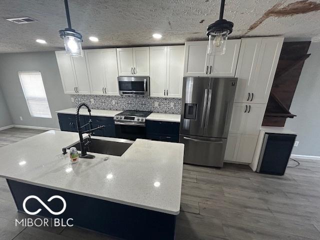 kitchen with pendant lighting, white cabinetry, appliances with stainless steel finishes, and a kitchen island with sink