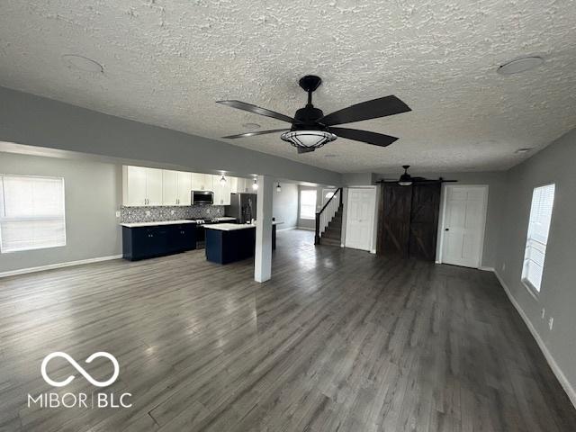 unfurnished living room with a wealth of natural light, dark wood-type flooring, a barn door, and ceiling fan