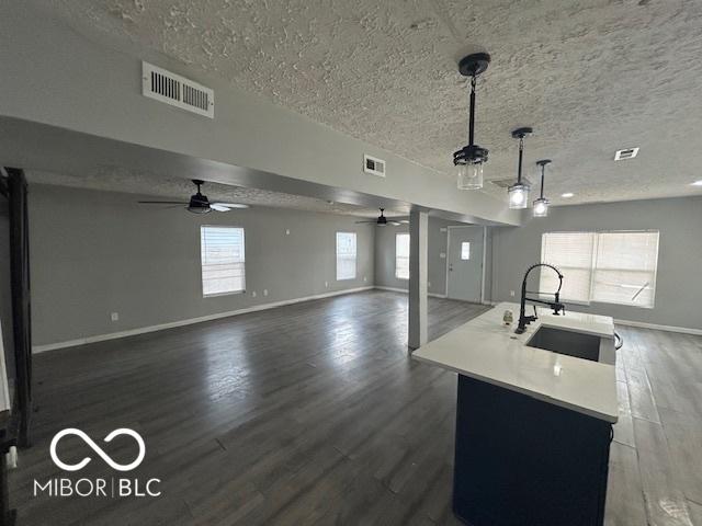 kitchen featuring sink, a textured ceiling, dark hardwood / wood-style floors, pendant lighting, and a kitchen island with sink