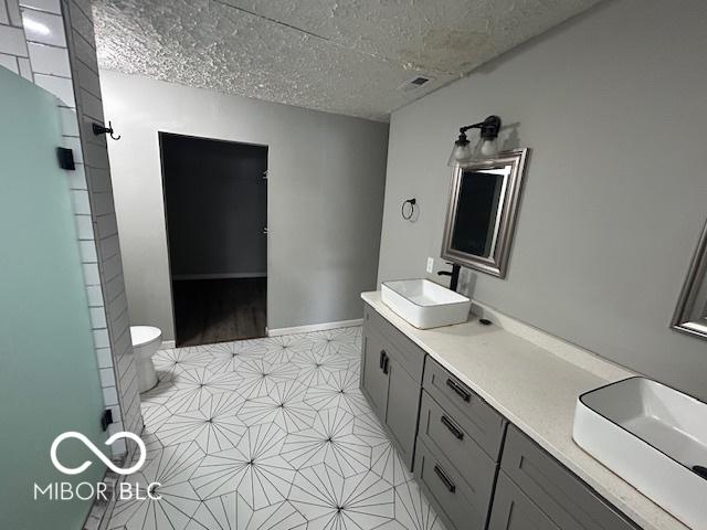 bathroom featuring vanity, toilet, an enclosed shower, and a textured ceiling