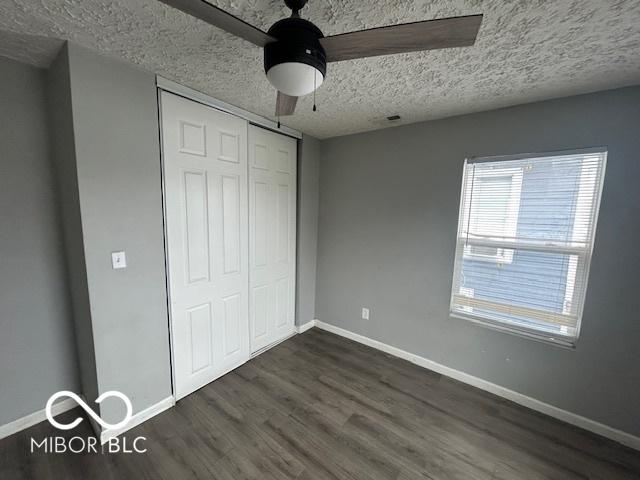 unfurnished bedroom with a textured ceiling, dark hardwood / wood-style floors, a closet, and ceiling fan