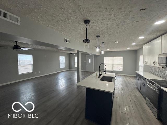 kitchen with a kitchen island with sink, white cabinetry, stainless steel appliances, dark hardwood / wood-style floors, and decorative light fixtures