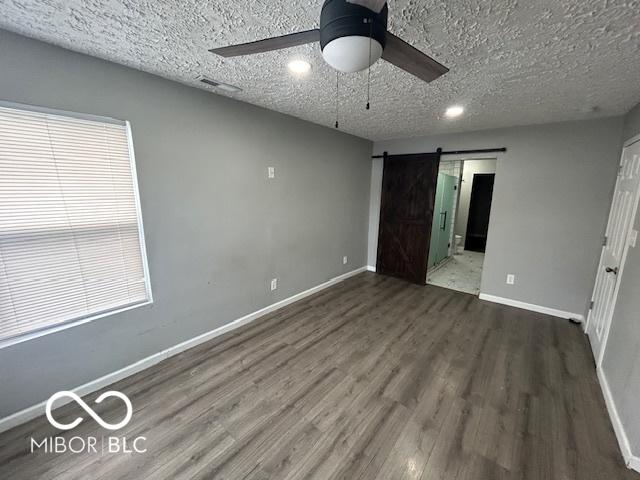 unfurnished bedroom with dark hardwood / wood-style floors, ceiling fan, a barn door, and a textured ceiling