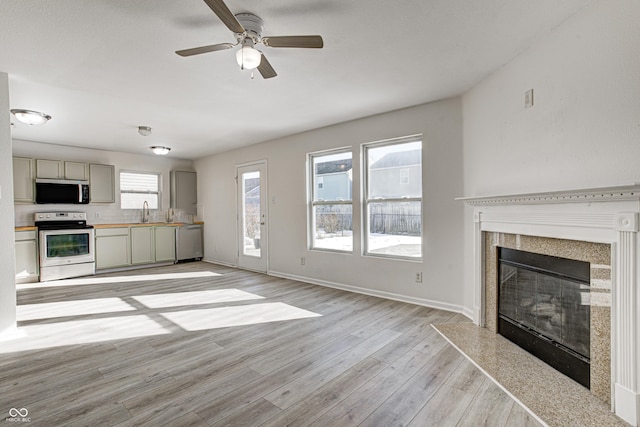 unfurnished living room featuring light wood-type flooring, sink, a premium fireplace, and ceiling fan