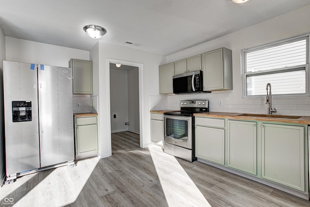 kitchen with sink, butcher block countertops, appliances with stainless steel finishes, and tasteful backsplash