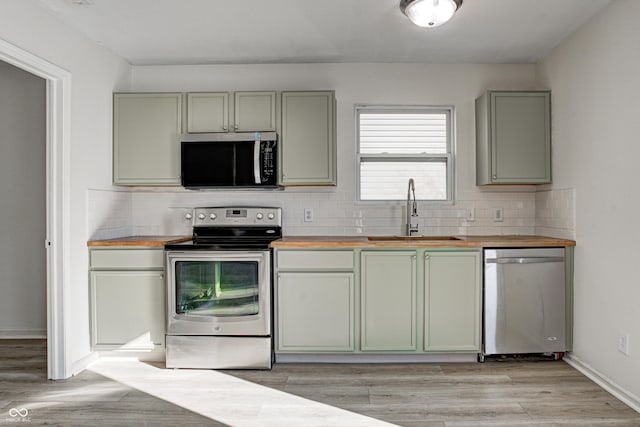 kitchen featuring tasteful backsplash, light hardwood / wood-style floors, butcher block countertops, sink, and stainless steel appliances