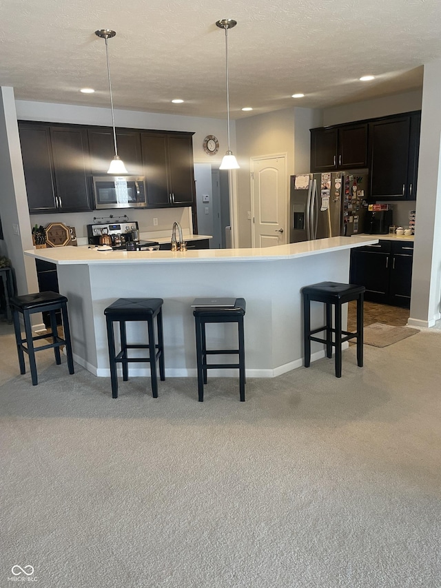 kitchen featuring light carpet, hanging light fixtures, stainless steel appliances, and an island with sink