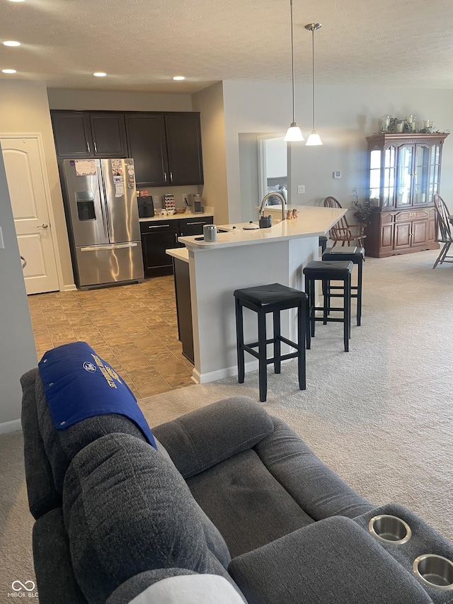 kitchen featuring pendant lighting, a breakfast bar area, light colored carpet, stainless steel fridge with ice dispenser, and a center island with sink