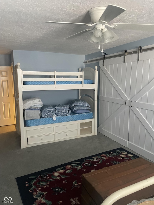 carpeted bedroom with ceiling fan, a barn door, and a textured ceiling