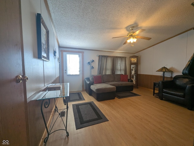 living room featuring hardwood / wood-style floors, wooden walls, ceiling fan, crown molding, and a textured ceiling